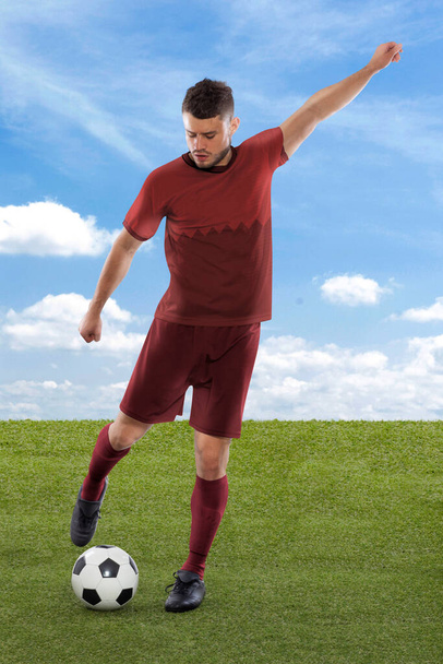 Jogador de futebol profissional com camisa vermelha da equipe nacional do Qatar prestes a marcar um gol com uma expressão de desafio e decisão em seu rosto no campo grama e nuvem de fundo - Foto, Imagem