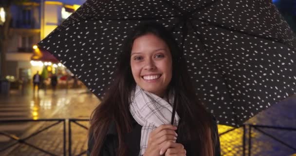 Turista en París por la noche durante una tormenta de lluvia sonriendo a la cámara. Mujer milenaria en la ciudad con paraguas de lunares. 4k - Metraje, vídeo