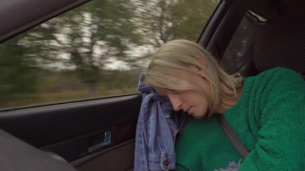 Woman with white hair and green sweater sleeps in car in front passenger seat. It is fastened with seat belt. Outside window landscape of fields and trees, ray of sun shines in camera. - Footage, Video