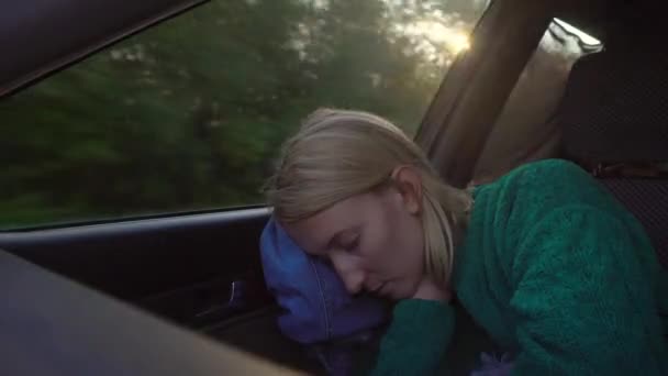 Woman with white hair and green sweater sleeps in car in front passenger seat. It is fastened with seat belt. Outside window landscape of fields and trees, ray of sun shines in camera. - Footage, Video