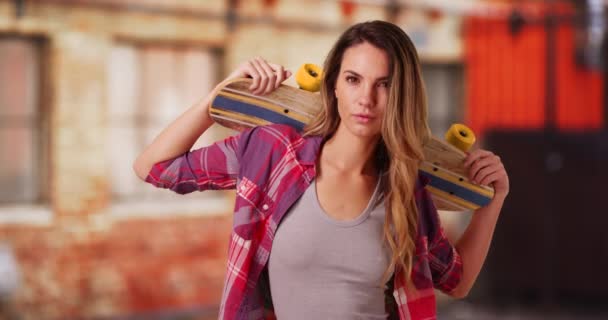 Portrait of white millennial girl posing with skateboard outdoors during the day. Portrait of trendy female skater holding skateboard on shoulders outside on the street. 4k - Footage, Video
