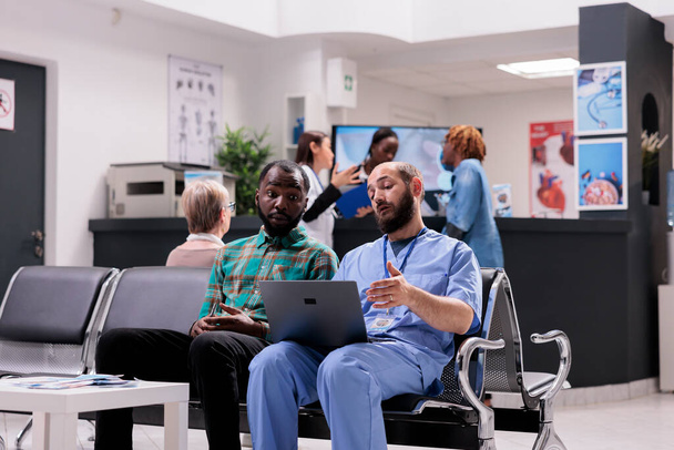 Afrikanischer Mann diskutiert Behandlungsmöglichkeiten für Familienmitglieder mit einem Chirurgen. Gesundheitsexperte zeigt dem Patienten am Computer radiologische Bilder. Menschen in medizinischer Einrichtung - Foto, Bild
