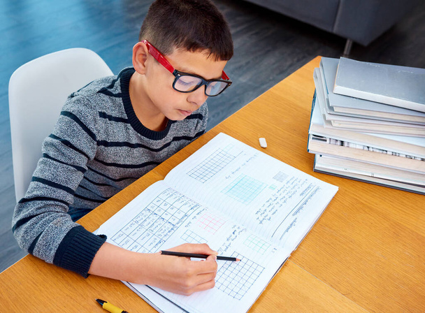 Hän tekee läksynsä yksin. päättäväinen nuori poika tekee kotiläksynsä kotona - Valokuva, kuva