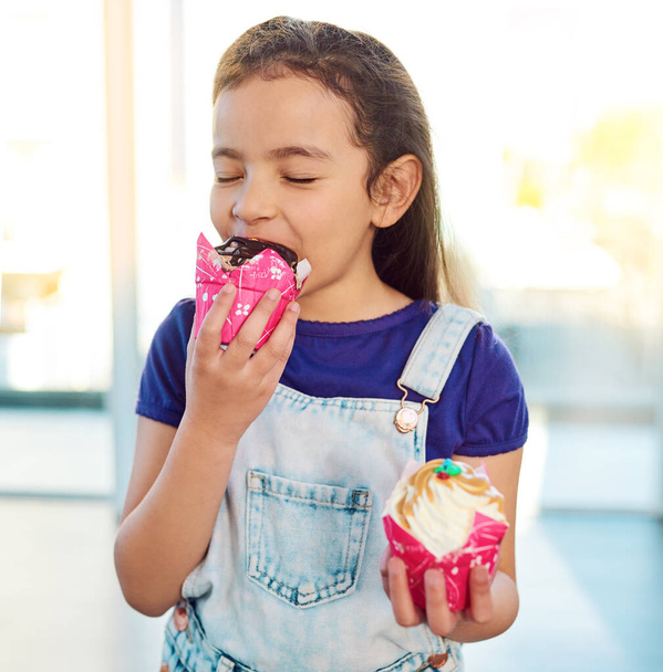 You can see the delight in her face. an adorable little girl eating a delicious cupcake at home - Foto, imagen