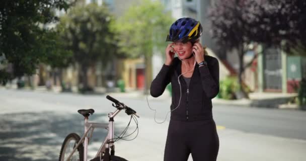 Femme caucasienne d'âge moyen en vêtements de sport en utilisant l'appareil post-entraînement sur la rue de la ville au centre-ville. Femme blanche sportive utilisant la technologie après l'exercice avec vélo pendant la journée. 4k - Séquence, vidéo
