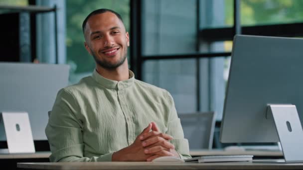 Feliz sorridente investidor masculino multirracial desenvolvedor programador designer criativo cara afro-americano homem com computador no escritório olhando para câmera sorriso sentado à mesa no local de trabalho da empresa - Filmagem, Vídeo