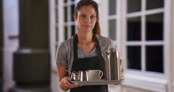 Die unglücklich attraktive Kellnerin trägt Tablett mit Kaffeegetränken. Müder Server, der Schürze trägt und Tablett hält, um Getränke zu servieren, blickt direkt in die Kamera. 4k - Filmmaterial, Video