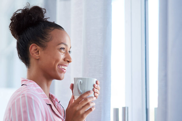 Café chaud et sourires vont ensemble le matin. une jolie jeune femme dégustant son café du matin à la maison - Photo, image