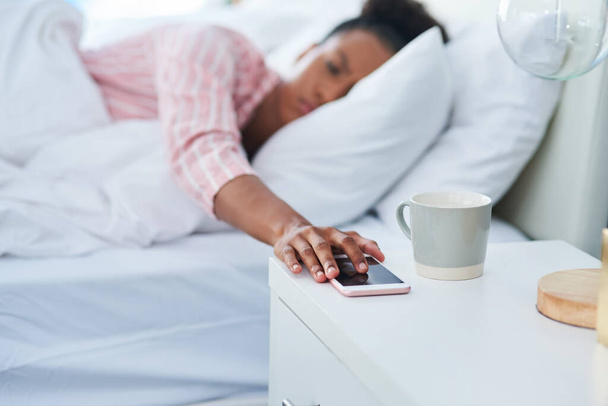 Дай мне еще раз вздремнуть. привлекательная молодая женщина в постели тянется к своему телефону на комоде дома - Фото, изображение