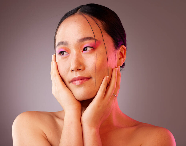 Face, beauty and makeup with a model asian woman in studio on a gray background to promote cosmetics. Wellness, luxury and eye shadow with a young woman touching her skin after cosmetic treatment. - Fotografie, Obrázek