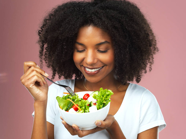 Menos dieta, más alimentación saludable. Captura de estudio de una atractiva joven mujer comiendo ensalada sobre un fondo rosa - Foto, imagen