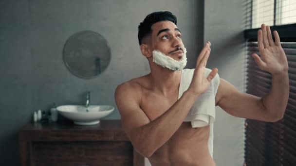 Humoros spanyol meztelen fickó borotvahabzselével az arcán táncol a fürdőszobában. Buta boldog gondtalan indiai latin férfi szakállas férfi borotválkozás előtt tánc mozgó kéz szórakozás zene vicces higiénia - Felvétel, videó