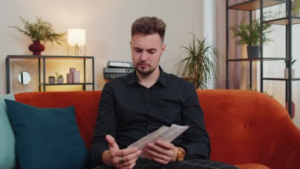 Stressed young man looking at unpaid bank debt bills, doing paperwork, planning budget, calculate finances mortgage payments. Displeased businessman guy at home throws paper bills sitting on couch - Footage, Video