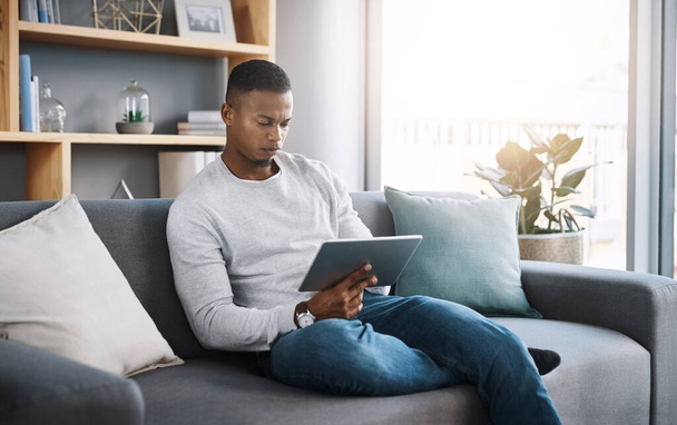 Este episodio se está poniendo muy intenso. un joven guapo usando su tableta digital mientras está sentado en un sofá en casa - Foto, Imagen