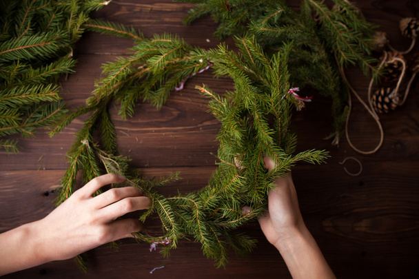 Κάνει Χριστούγεννα στεφάνι με τα χέρια σε ξύλινα φόντο - Φωτογραφία, εικόνα