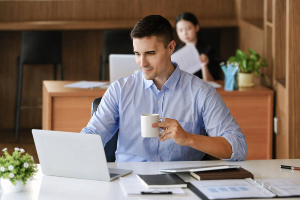 Gerentes de marketing do sexo masculino bebem café enquanto trabalham para reduzir a sonolência antes de usar computadores, iPads e documentos de análise de marketing - Foto, Imagem
