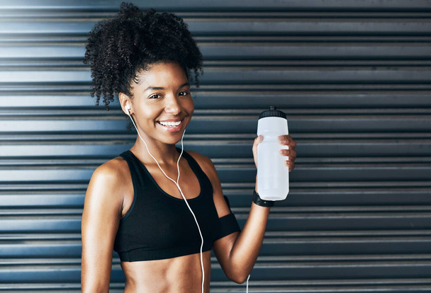 Edzés közben mindig legyen egy üveg az oldaladon. Portré egy sportos fiatal nő ivóvíz, miközben gyakorolja a szürke háttér - Fotó, kép