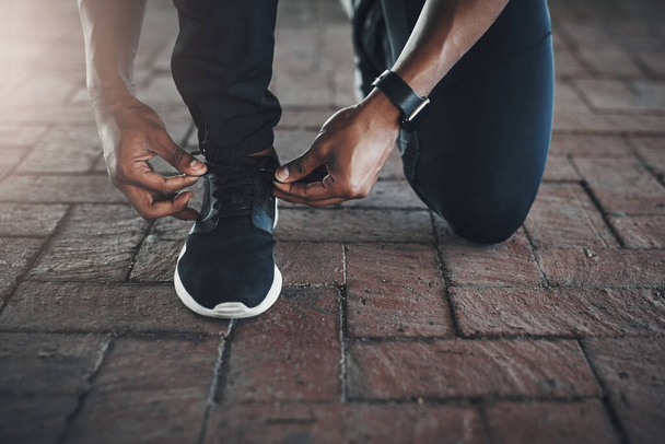 Lacing up for the road ahead. an unrecognizable young man tying his laces while exercising outside - 写真・画像