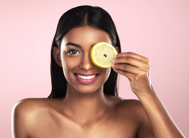 De krachten van vitamine C zijn geen geheim. Studio portret van een mooie jonge vrouw poseren met een oranje plak tegen een roze achtergrond - Foto, afbeelding