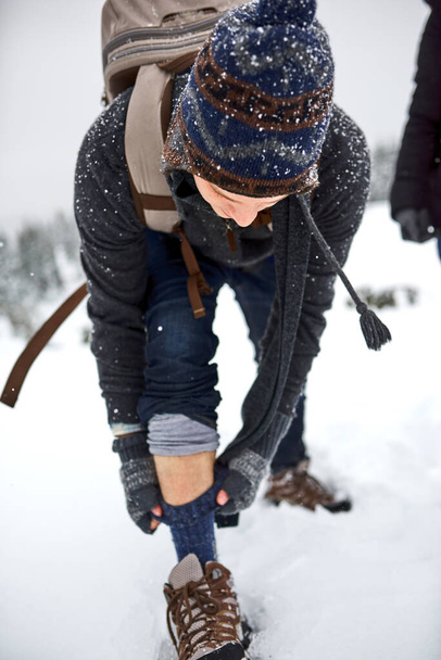 Im as warm as can be. a young man pulling up his socks while out on the snow - Фото, изображение