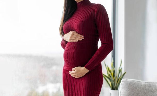 Pregnant woman profile holding her belly in red dress. Beautiful model for pregnancy maternity clothes. - Foto, immagini