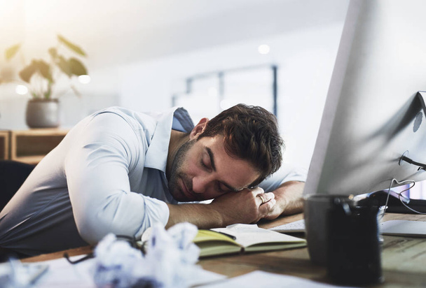 Im juts gaat mijn ogen sluiten voor 2 minuten... een jonge zakenman slapen aan zijn bureau, terwijl werken laat in een kantoor - Foto, afbeelding