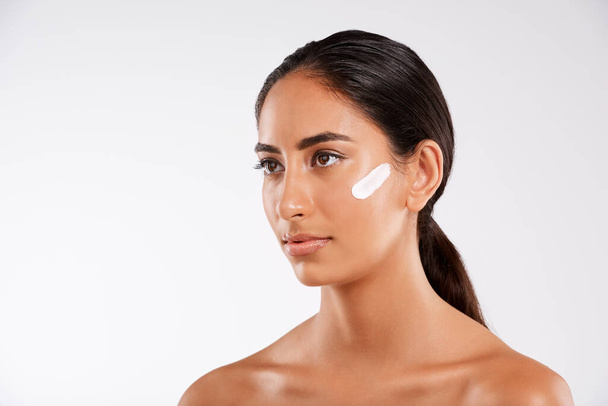 Silky, smooth and flawless. Studio shot of a beautiful young woman posing with lotion on her face against a gray background - Foto, Imagem