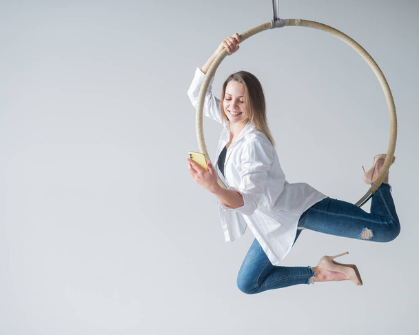 Caucasian female gymnast doing aerial hoop exercises and using smartphone - Foto, Bild