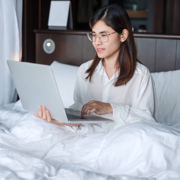 İş için dizüstü bilgisayar kullanan mutlu bir kadın. Yatakta bilgisayarla buluşan bir kadın. teknoloji, ağ, evden çalışma, yaşam tarzı ve dijital iletişim kavramı - Fotoğraf, Görsel