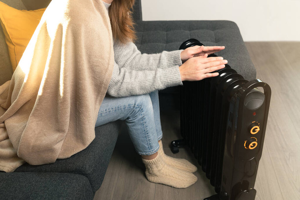 Women sitting and warming hands over and electric heater. High energy prices and cold home. - Foto, Imagem