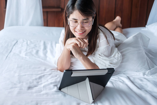 Mujer feliz usando la tableta para las redes sociales, joven mujer viendo películas en la almohadilla de la computadora en la cama en casa. tecnología, red, compras en línea, comercio electrónico, estilo de vida y concepto de comunicación digital - Foto, Imagen