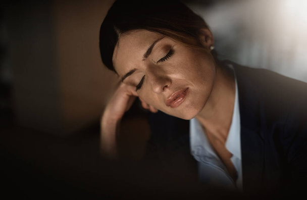 Misschien als ik een dutje doe aan mijn bureau... een jonge zakenvrouw die in slaap valt aan haar bureau tijdens een late nacht in een modern kantoor. - Foto, afbeelding