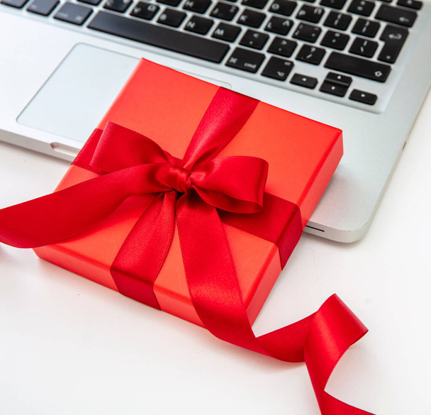 Red gift box and computer laptop on white background, close up view. Christmas presents Online shopping template - Photo, Image