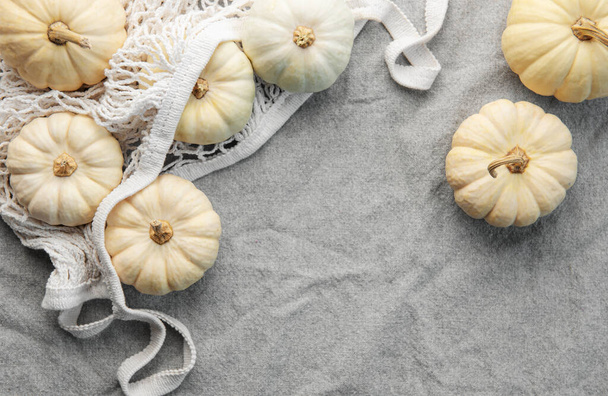 Top view őszi kompozíció sütőtök hálós bevásárló zsák szürke textil háttér - Fotó, kép