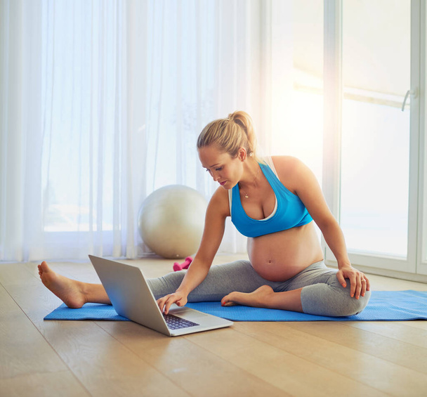 Ella es una bloguera de fitness del embarazo. una mujer embarazada usando una computadora portátil durante un entrenamiento en casa - Foto, imagen
