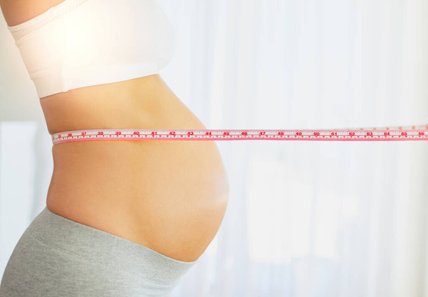 Bebé en progreso. una mujer embarazada midiendo su vientre en casa - Foto, Imagen