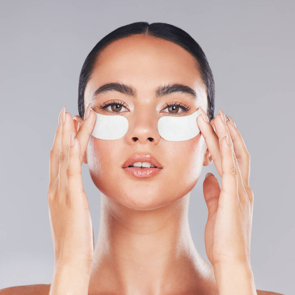 Face, skincare and woman with eye patches on a gray studio background. Portrait, beauty and model from Canada with facial collagen pads or dermatology product for anti aging, hydration or wellness - 写真・画像