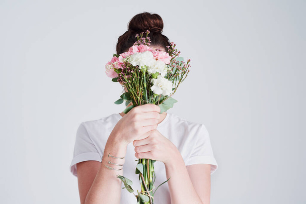 There is power in flowers. Studio shot of an unrecognizable woman covering her face with flowers against a grey background - Foto, afbeelding