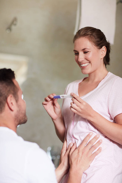 We gaan naar ouders. een vrouw tonen haar man een zwangerschapstest in de badkamer thuis - Foto, afbeelding