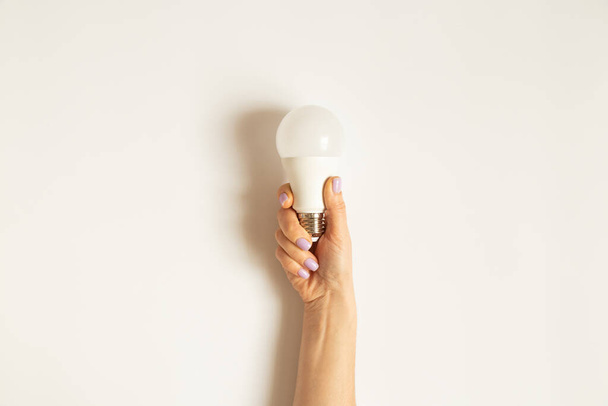 Светодиодная лампочка в руке девушки на белом фоне, электричество и экономия - Фото, изображение