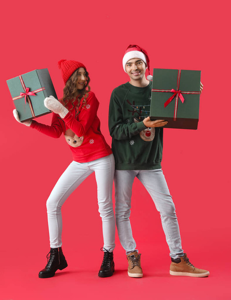 Νεαρό ζευγάρι ερωτευμένο με χριστουγεννιάτικα δώρα σε κόκκινο φόντο - Φωτογραφία, εικόνα