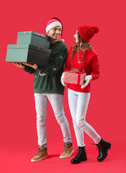 Jeune couple amoureux de cadeaux de Noël sur fond rouge - Photo, image