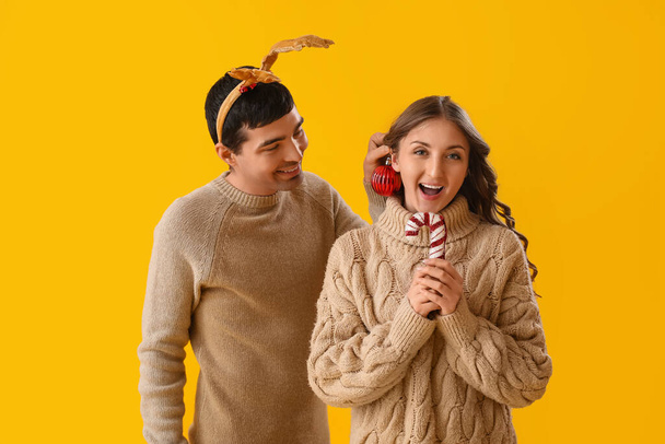 Junges verliebtes Paar mit Weihnachtsdekor auf gelbem Hintergrund - Foto, Bild