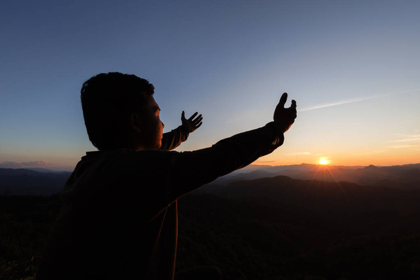 silhouet van een man Handen bidden met geloof in religie en geloof in God Op de ochtend zonsopgang achtergrond. Gebedshouding. - Foto, afbeelding