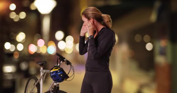 Femme caucasienne d'âge moyen en tenue de sport allant faire du vélo au centre-ville le soir. Femme blanche sportive se préparant à faire du vélo dans la rue de la ville la nuit. 4k - Séquence, vidéo