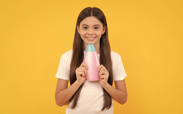 happy child holding shampoo bottle on yellow background, cosmetic. - Фото, зображення
