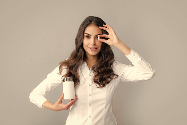 Здравоохранение и медицина. Портрет привлекательной девушки, держащей на бутылке таблетки здорового продукта на сером фоне - Фото, изображение