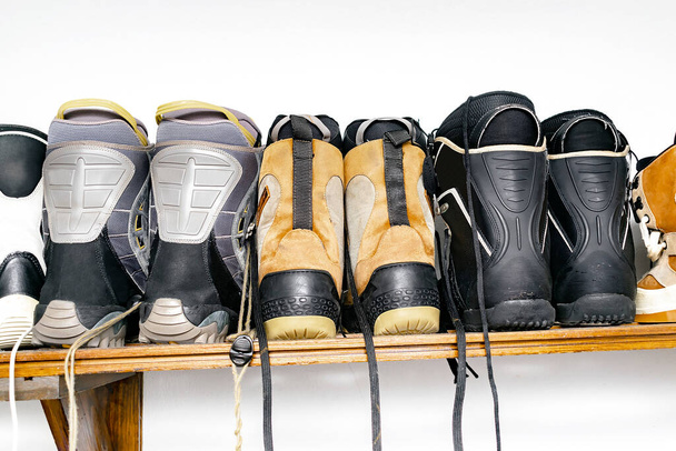 Botas de snowboard, de pie, colgadas en un soporte de pared de madera personalizado en el almacén para almacenamiento estacional en la estación de esquí alpino. Manipulación extrema de equipos deportivos de invierno en casa - Foto, Imagen