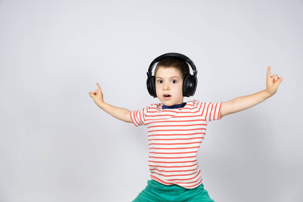 Happy boy in headphones and t-shirt points his fingers up on a white background. - Фото, изображение