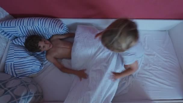 Kind springt ins Bett. Glückliche Geschwister schwelgen unter Bettlaken - Filmmaterial, Video